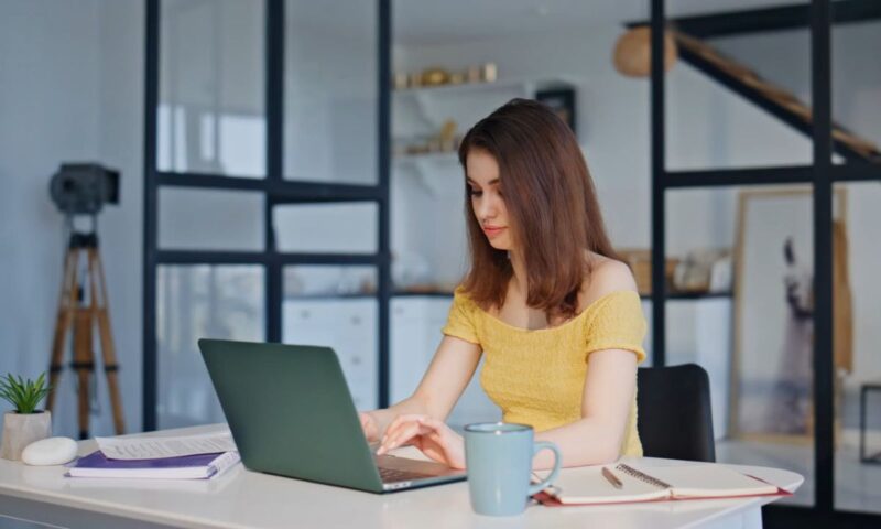 devojka sedi za stolom i radi za svojim laptopom