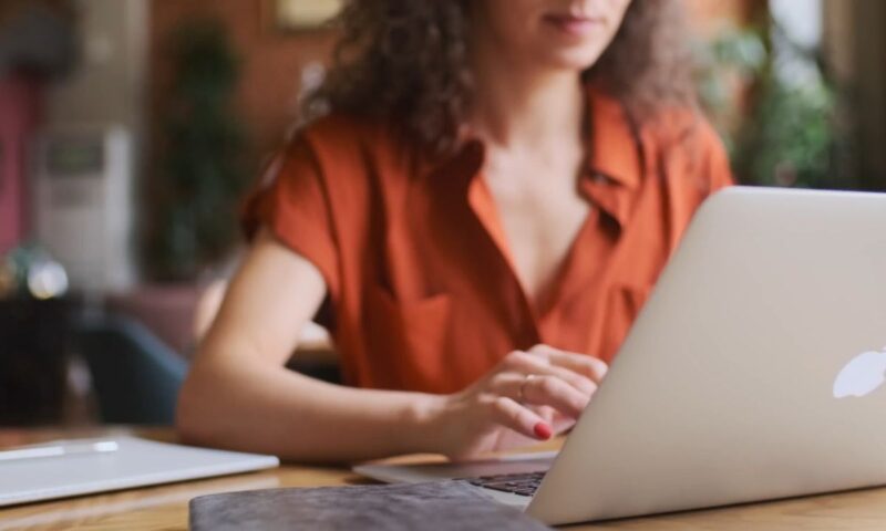 devojka sedi za stolom i koristi svoj apple laptop